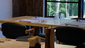 Un salón de conferencias con una larga mesa, sillas y vistas a árboles a través de un amplio ventanal.