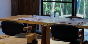 Un salón de conferencias con una larga mesa, sillas y vistas a árboles a través de un amplio ventanal.
