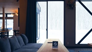 Een modern interieur met een bank, een houten tafel en grote ramen met uitzicht op een besneeuwd landschap.