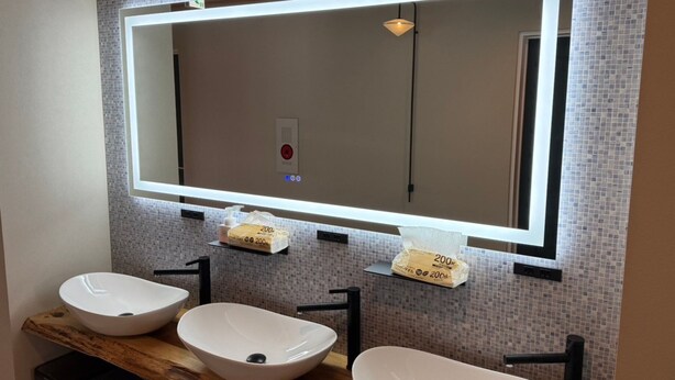 A bathroom with two vessel sinks, a large mirror, and a wall-mounted light fixture. - ChillSheep (Suzaka)