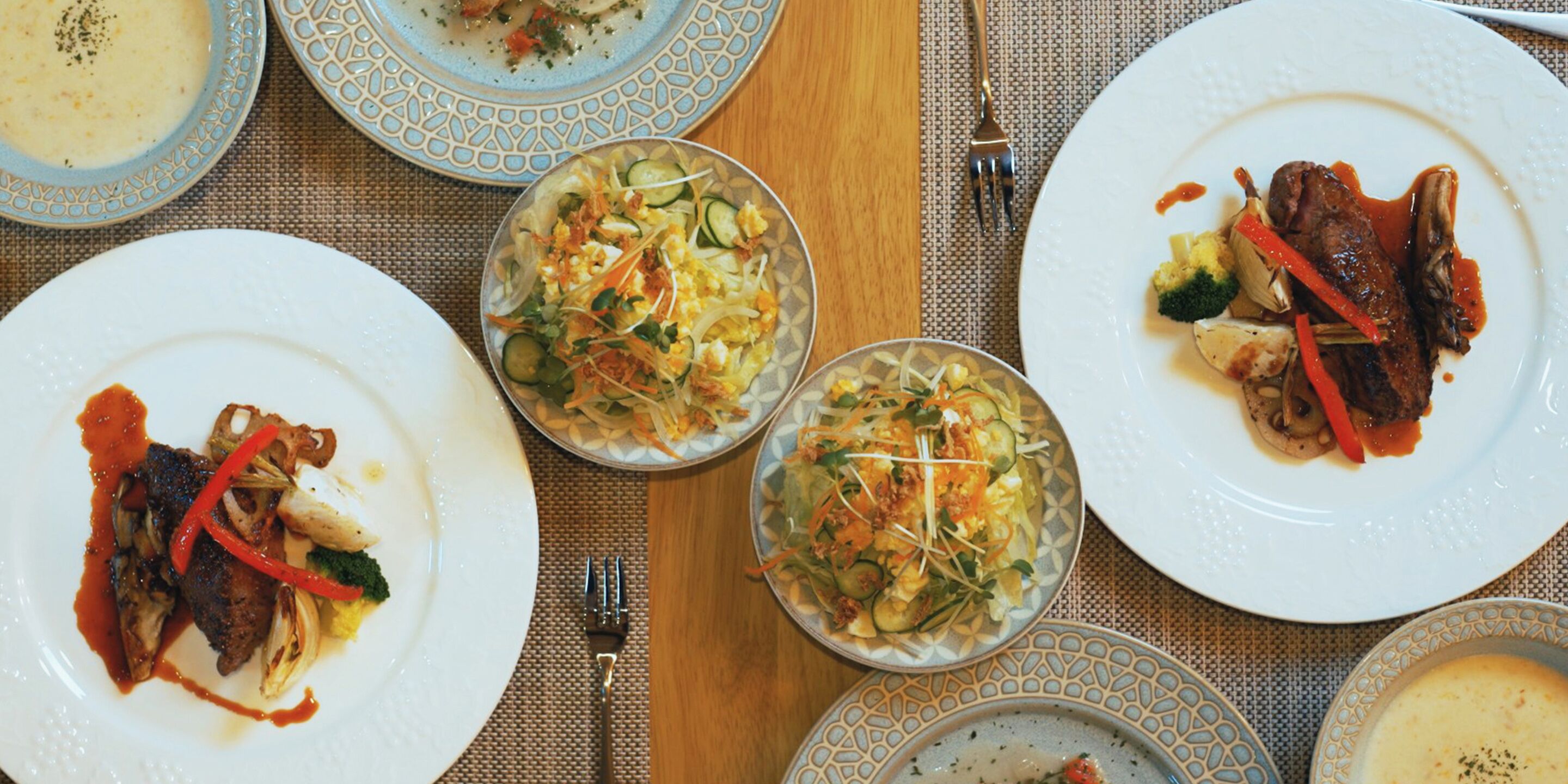 Una mesa servida con platos de comida, incluyendo carne, verduras y sopa.