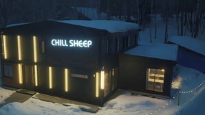 Un edificio moderno con un letrero de neón que dice "CHILL SHEEP" y luces verticales iluminadas.