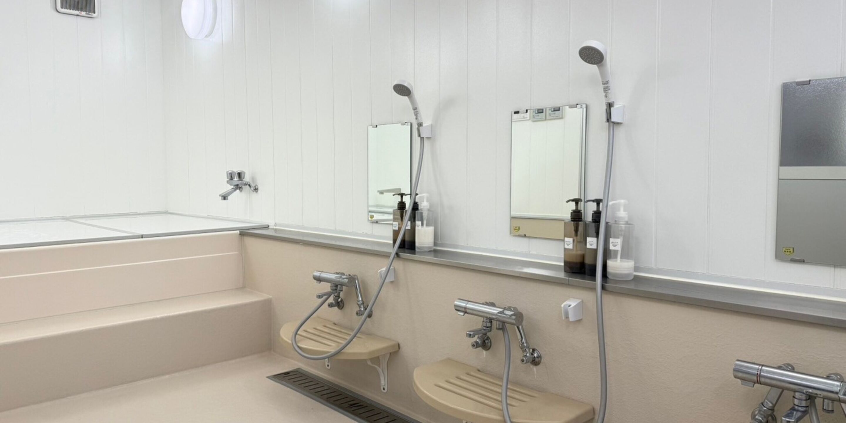 Een moderne badkamer met een grote spiegel, twee wastafels, een douche en een toilet.