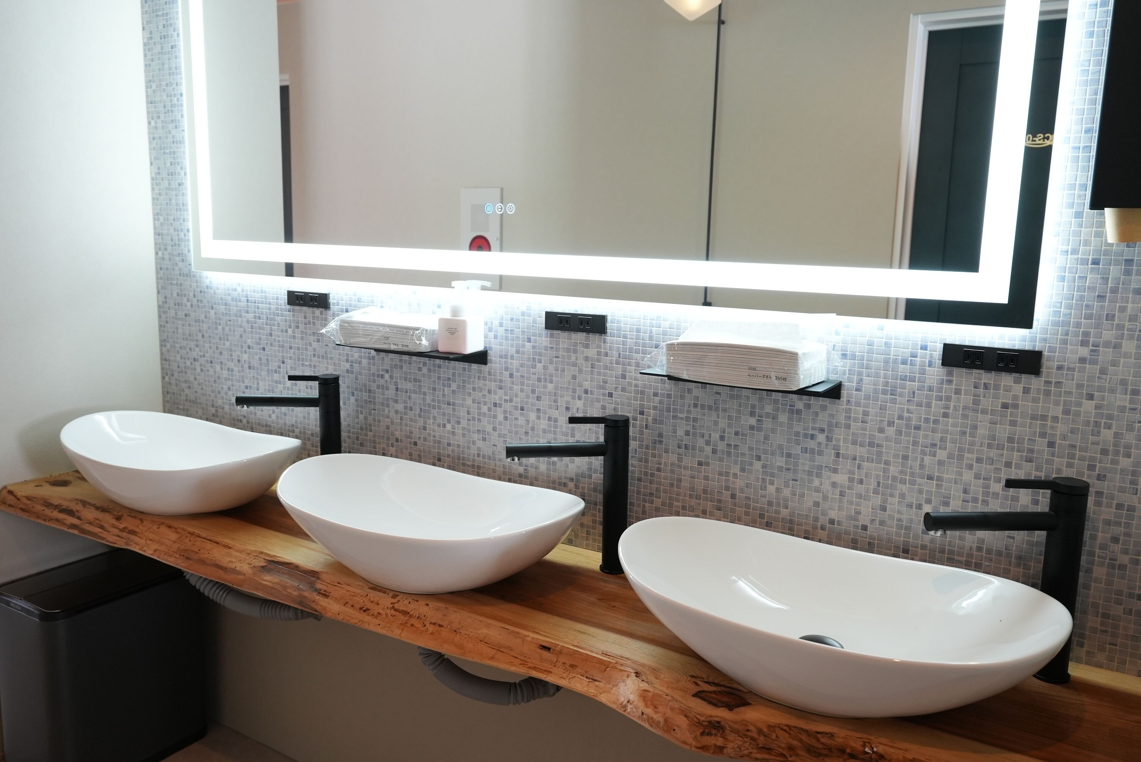 A bathroom with three white vessel sinks, black faucets, and a wooden vanity.