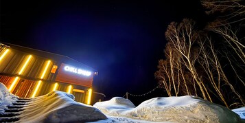 A building with a 'CHILI SHOP' sign at night, surrounded by snow and bare trees.