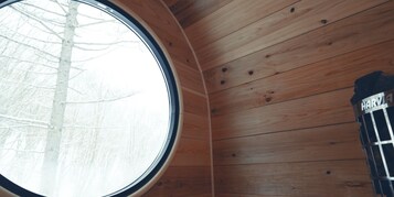 Interior de una cabaña de madera con un amplio ventanal circular, techo de madera visible y una estructura metálica con la etiqueta 'HARV'.