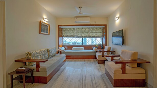 A modern living room with a sofa, two armchairs, a coffee table, and a TV. - Yellowbrick-Calcutta's Freshest BnB (Kolkata)