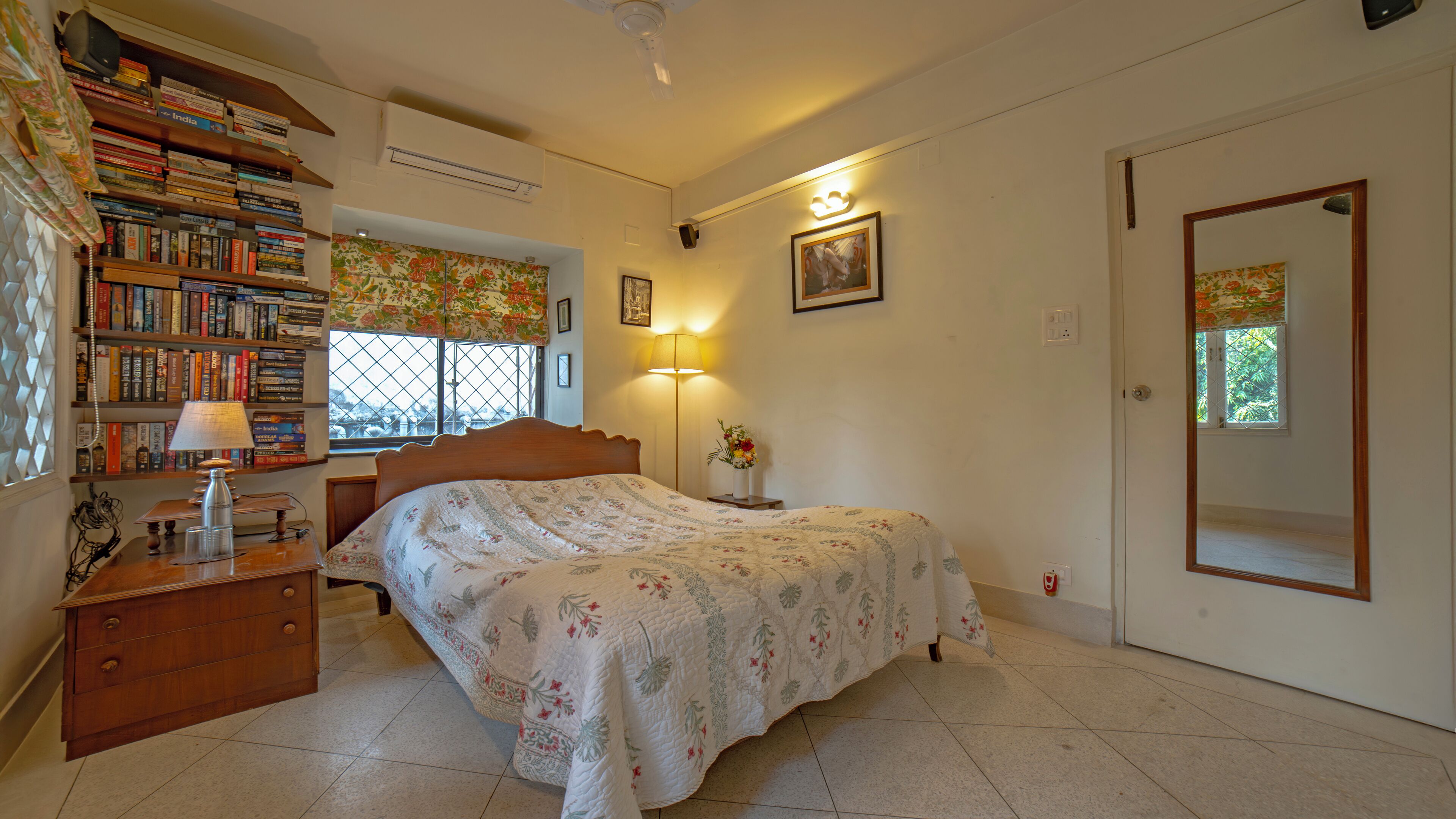 Une chambre à coucher comprenant un lit, une table de chevet, une lampe, une bibliothèque et une fenêtre donnant sur un beau paysage.
