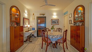 A dining room with a round table, chairs, wooden cabinets, and a ceiling fan. - Yellowbrick-Calcutta's Freshest BnB (Kolkata)
