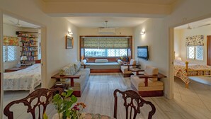 A spacious living room with a sofa set, a coffee table, and a TV mounted on the wall. There is a bookshelf filled with books and a window with a decorative screen. - Yellowbrick-Calcutta's Freshest BnB (Kolkata)