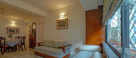 A living room with a sofa, a dining table with chairs, a ceiling fan, and a window with curtains.