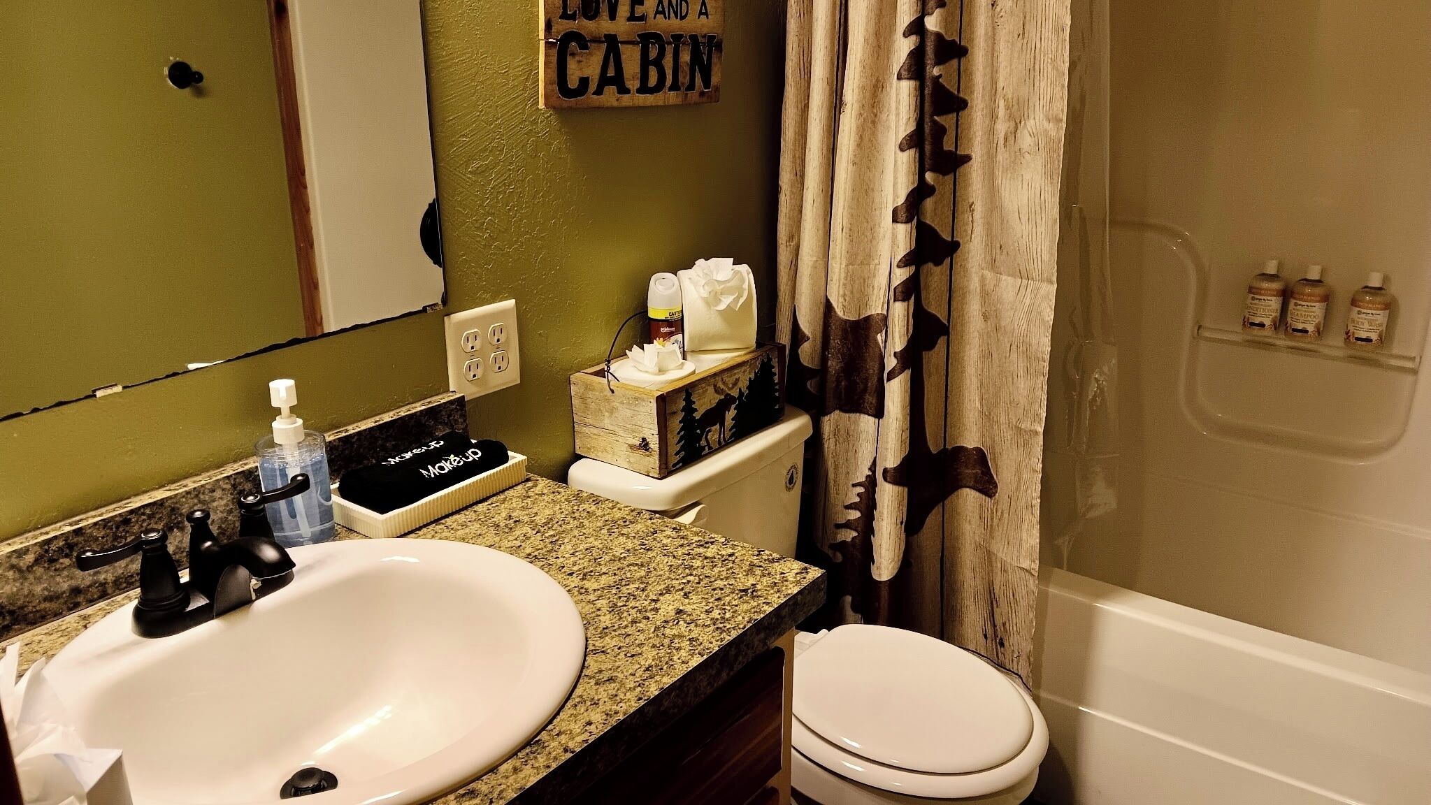 A bathroom with a sink, toilet, and shower. There is a sign on the wall that reads "Love and a Cabin."