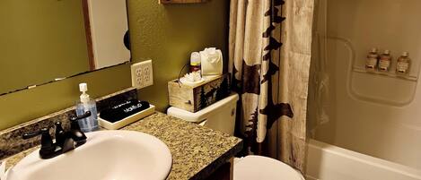 A bathroom with a sink, toilet, and shower. There is a sign on the wall that reads "Love and a Cabin."