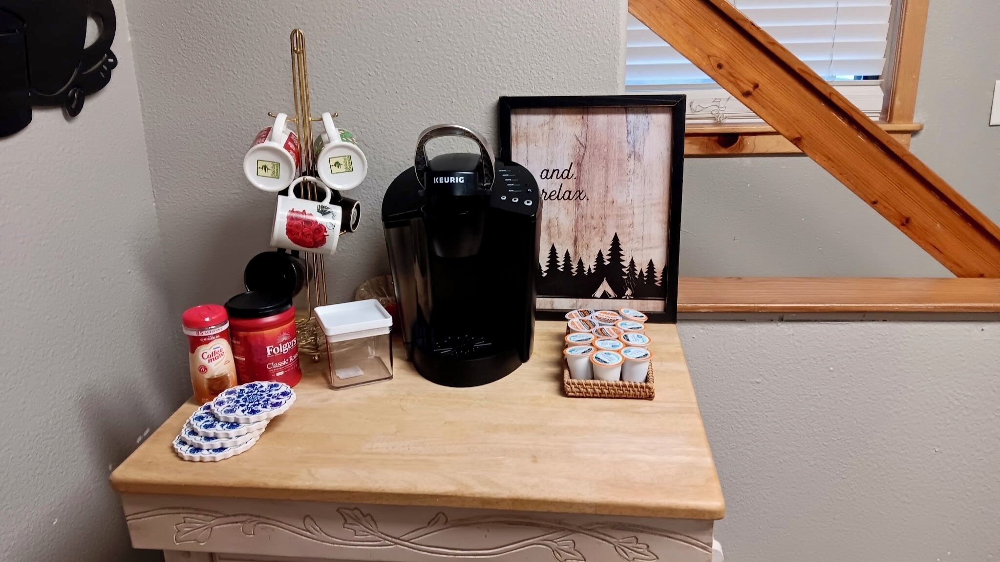 Una estación de café con una cafetera Keurig, café Folgers, una jarra de café y un cesto de tazas de café.
