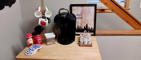 Una estación de café con una cafetera Keurig, café Folgers, una jarra de café y un cesto de tazas de café.