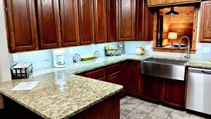 Una cocina con encimeras de granito, gabinetes de madera, un lavamanos de acero inoxidable y una cafetera.