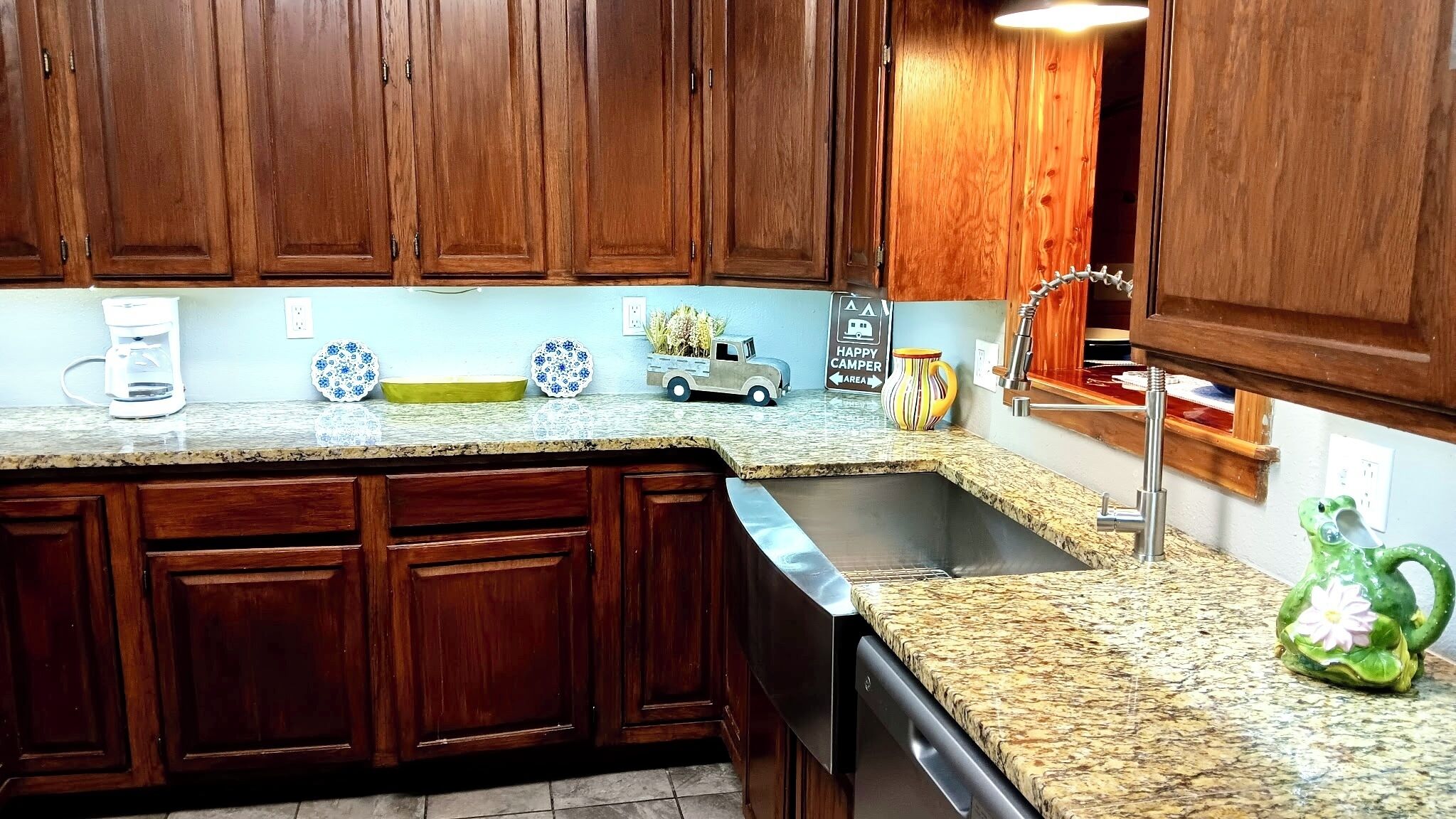 A kitchen with wooden cabinets, granite countertops, a coffee maker, decorative plates, a toy truck, and a frog-shaped vase.