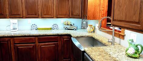 A kitchen with wooden cabinets, granite countertops, a coffee maker, decorative plates, a toy truck, and a frog-shaped vase.