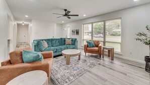 A spacious living room with a teal sofa, a brown sofa, a round coffee table, and a ceiling fan.