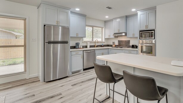 A modern kitchen with light gray cabinets, stainless steel appliances, and a central island with bar stools.