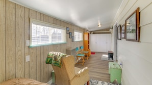 A room with wooden panel walls, a bed, a chair, a table, and a window with blinds. - Farmhouse w/ Horse Corral Near Wind River Arena (Rigby)