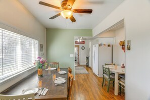 A dining area with a wooden table set for four, a ceiling fan, and a view through a window with blinds. - Farmhouse w/ Horse Corral Near Wind River Arena (Rigby)