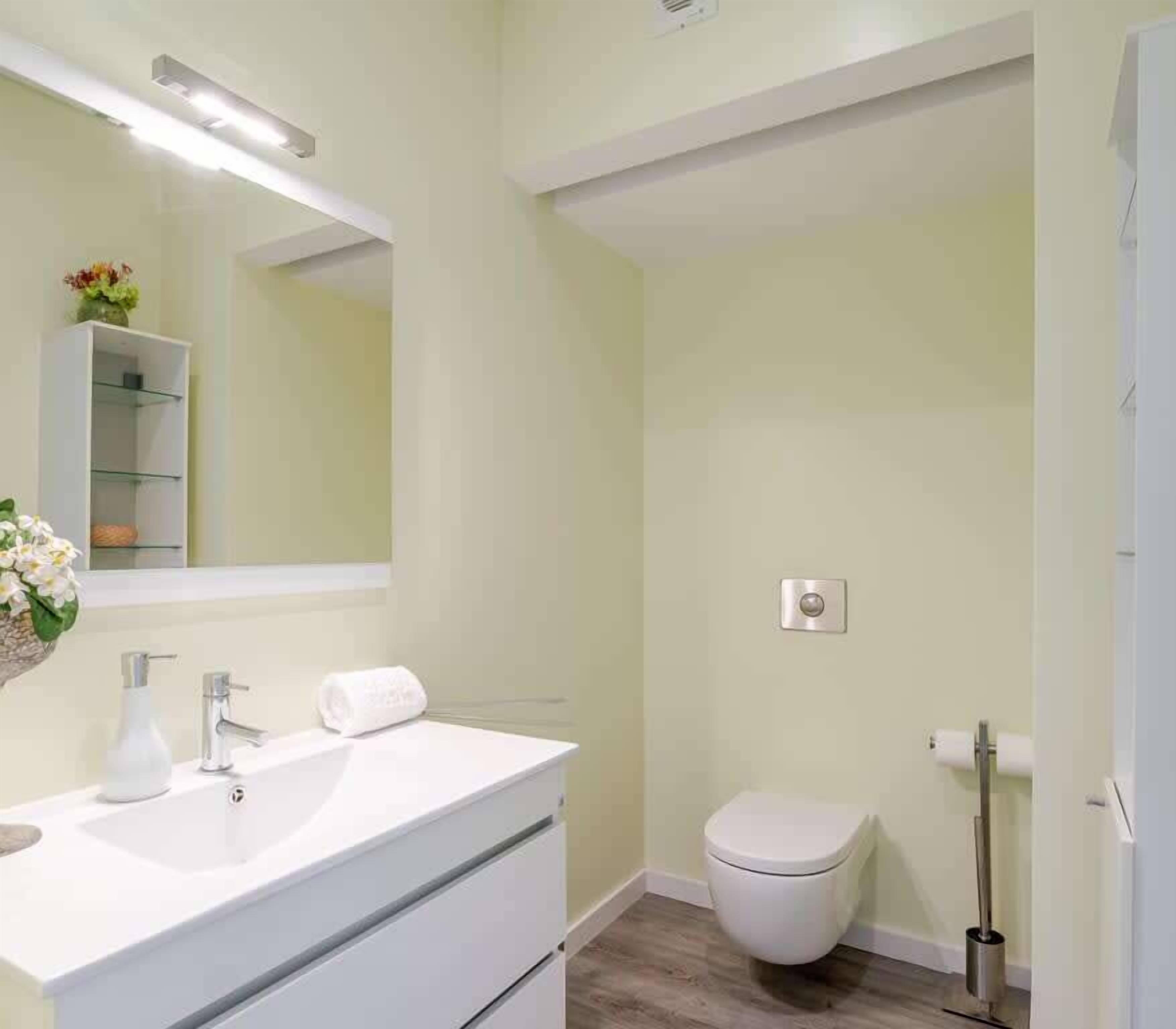A bathroom with a white sink, mirror, toilet, and a shower area.