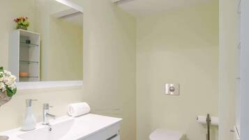 A bathroom with a white sink, mirror, toilet, and a shower area.