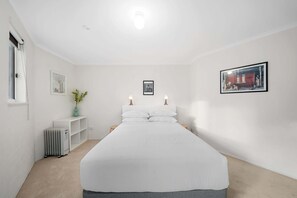 Ein schlicht eingerichtetes Schlafzimmer mit einem großen Bett, einem Heizkörper, einem kleinen Tisch und einem Fenster.
