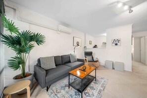 Ein modernes Wohnzimmer mit grauem Sofa, einem Holztisch und einer Topfpflanze.