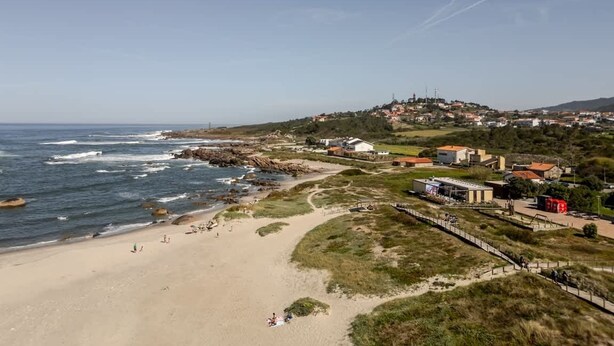 Eine Küstenstadt mit Strand, Gebäuden und einer hügeligen Landschaft im Hintergrund.