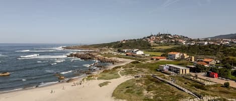 A coastal town with a beach, buildings, and a hilly backdrop.