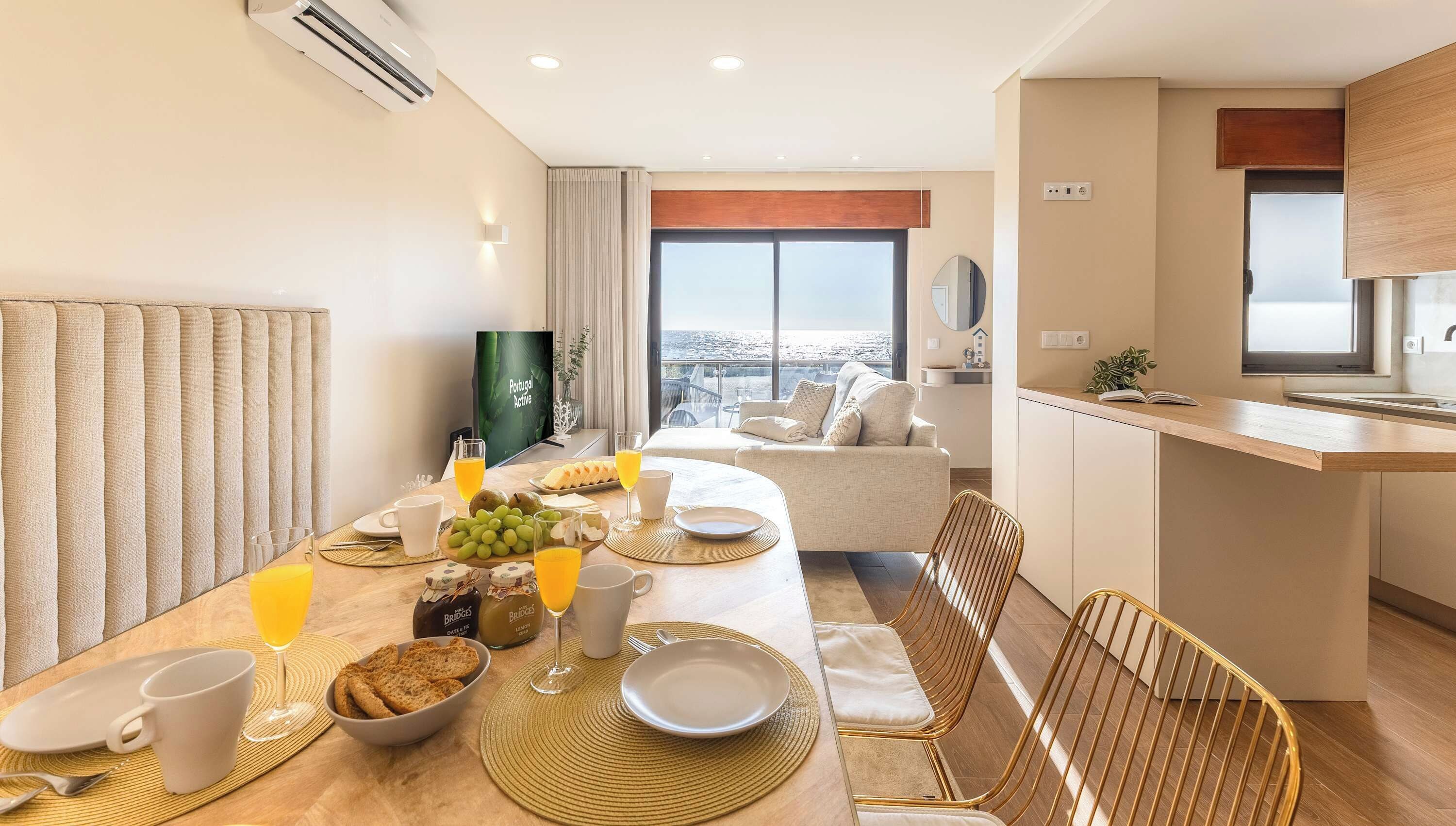 Une chambre d’hôtel équipée d’une table à manger dressée pour le petit-déjeuner, d’un canapé, d’un coin cuisine et d’une grande fenêtre donnant sur la ville.