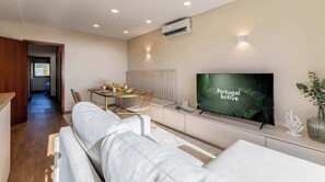 A modern living room with a sofa, a dining table with chairs, a television, and an air conditioning unit.