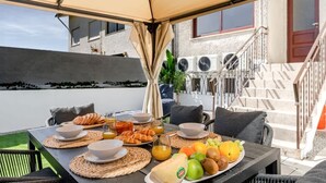 Ein Essbereich im Freien mit einem für das Frühstück gedeckten Tisch, mit Croissants, Obst und Saft.
