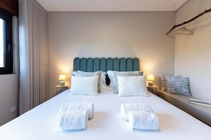 A hotel room with a large bed, two bedside lamps, a headboard, and a window with curtains.