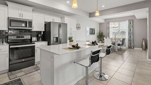 A modern kitchen with white cabinetry, stainless steel appliances, and a central island with bar stools. - Cozy & Stylish 2BR Condo, Prime Storey Lake Spot (Kissimmee)