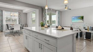 A modern kitchen with a large island, dining area, and a view of the outdoors. - Cozy & Stylish 2BR Condo, Prime Storey Lake Spot (Kissimmee)