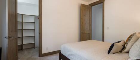 Un dormitorio con cama, una puerta de madera y un armario con estantes.