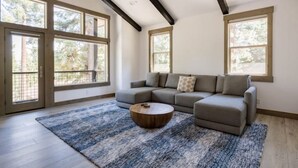 Ein modernes Wohnzimmer mit einem Ecksofa, einem runden Couchtisch und großen Fenstern mit Blick auf Bäume.