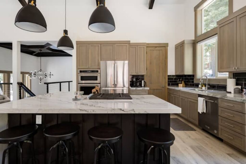 Una cocina moderna con una isla grande, taburetes de bar, iluminación colgante y armarios de madera.
