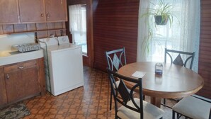 Une cuisine compacte avec des meubles en bois, un lave-linge, une table à manger avec des chaises et une fenêtre agrémentée d’une plante.