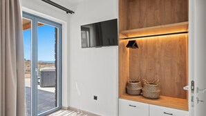 Ein modernes Zimmer mit einer Schiebeglas-Tür, die auf einen Balkon führt, einem an der Wand befestigten Fernseher und einem Holzregal mit Körben.