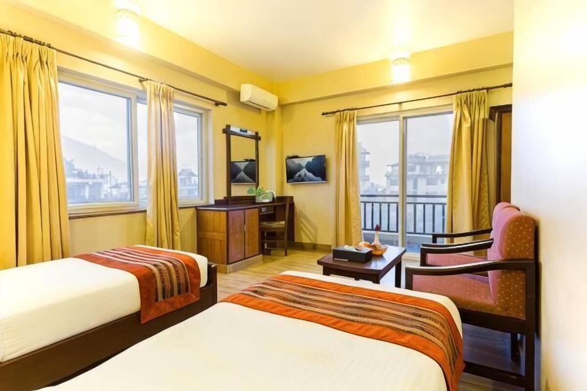 A hotel room with two beds, a desk, a chair, and a TV.