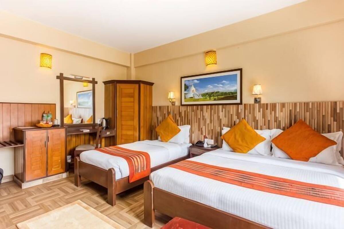 A hotel room with two beds, a desk, a wardrobe, and a painting on the wall.