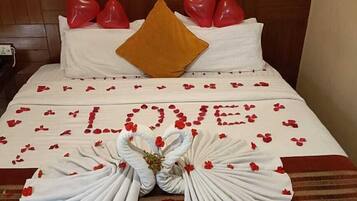 A bed with a heart-shaped pillow arrangement, a large 'LOVE' decoration made of rose petals, and a bouquet of flowers.