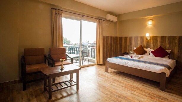 Une chambre d’hôtel avec un lit, une chaise, une table et un balcon avec des rideaux.