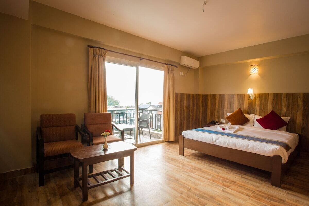 A hotel room with a bed, a chair, a table, and a balcony with curtains.