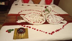 Un lit décoré de pétales de rose disposés en forme de cœur, deux cygnes faits avec des serviettes et un gâteau au chocolat sur lequel est écrit « Joyeuse lune de miel ».