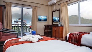 Une chambre d’hôtel avec deux lits, une télévision, un bureau avec une chaise et une vue sur un paysage montagneux.